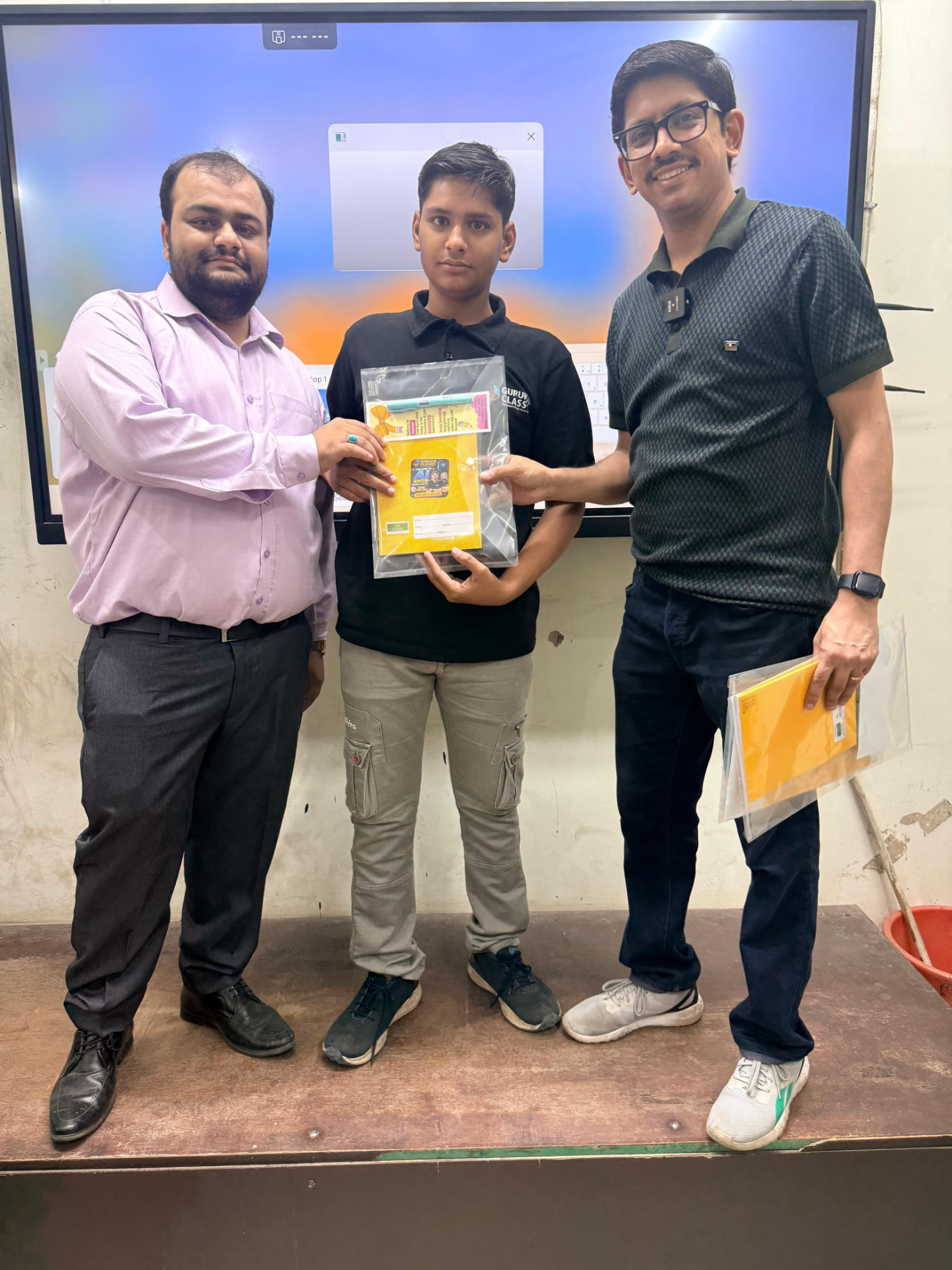 Student in a Gurukul Classes t-shirt receiving a study kit from faculty