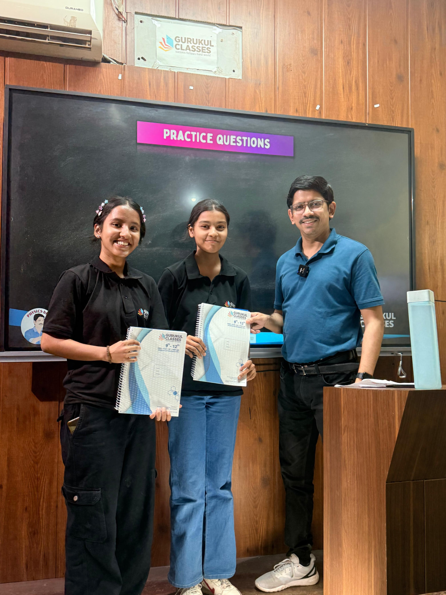 Two students receiving Gurukul Classes practice question booklets from Vaibhav Agarwal