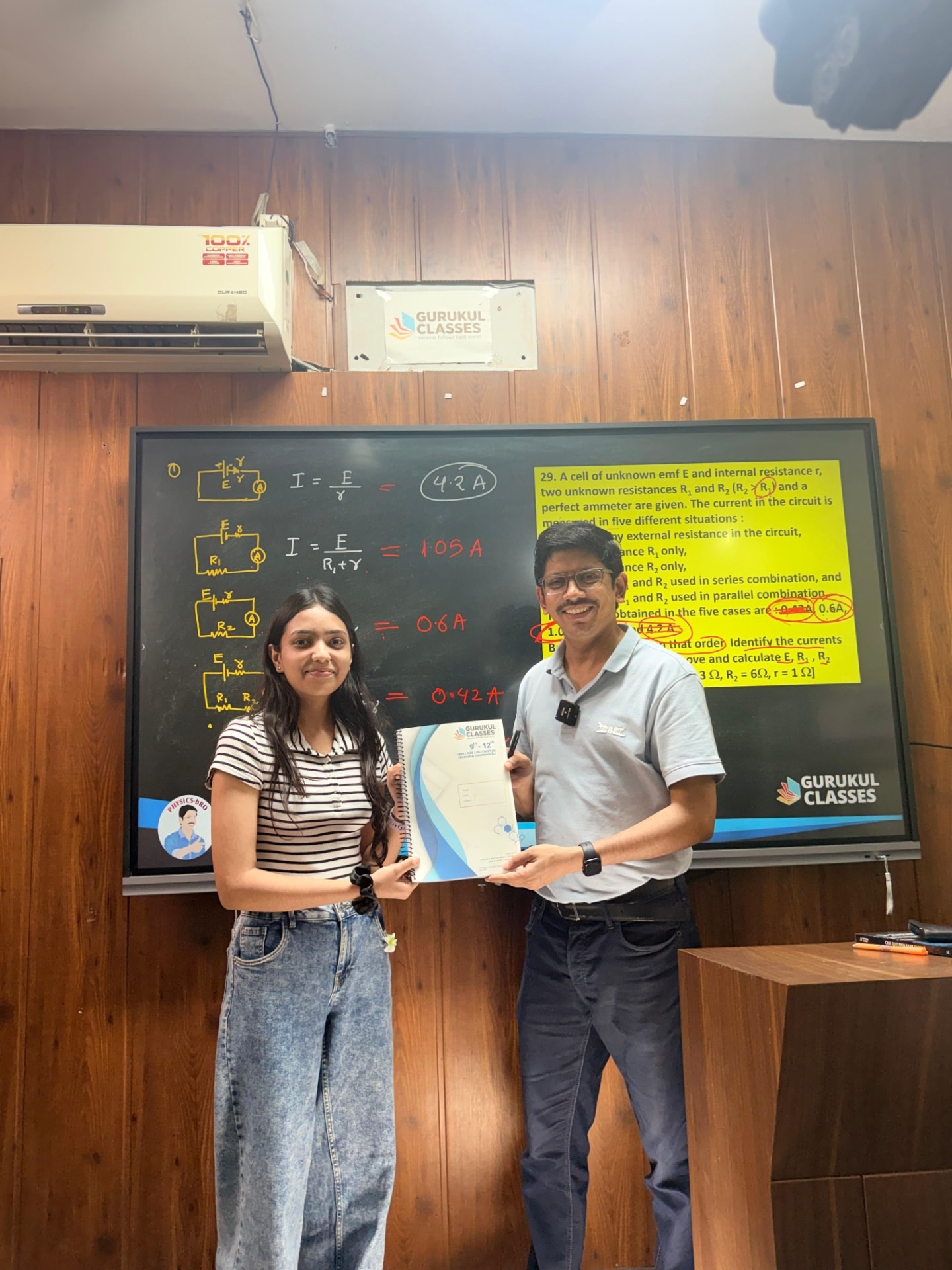 Student receiving Gurukul Classes notes from Vaibhav Agarwal during a current electricity lecture